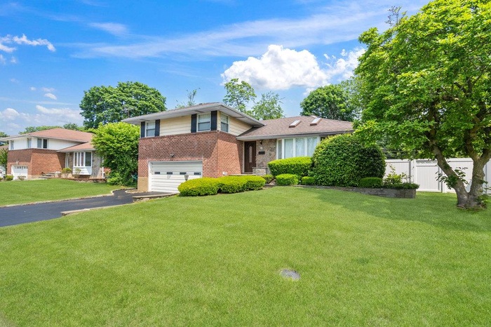 Tri-level home with brick siding, an attached garage, and driveway