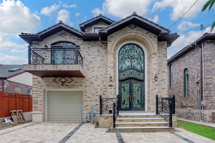 View of front of property featuring french doors, a balcony, an attached garage, and brick siding