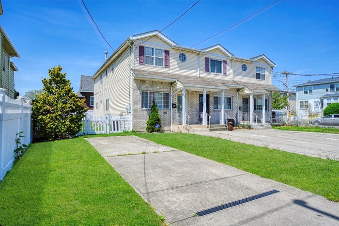 View of front of house with brick siding, fence, covered porch, a front yard, and a gate