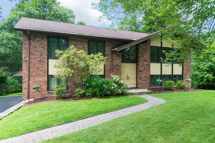 View of front of house with roof with shingles, a front yard, and brick siding