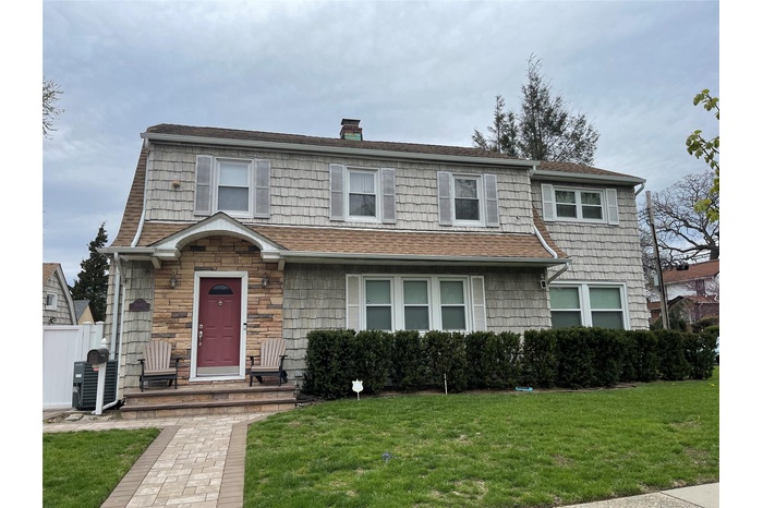 View of front of home featuring a front lawn, a chimney, roof with shingles, and central AC