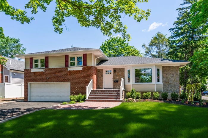 Split level home with a front lawn, driveway, an attached garage, and brick siding
