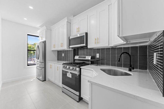 Kitchen with stainless steel appliances, tasteful backsplash, white cabinetry, light stone counters, and light tile patterned floors