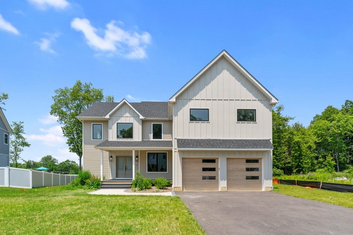 View of front facade featuring board and batten siding, roof with shingles, asphalt driveway, and a garage