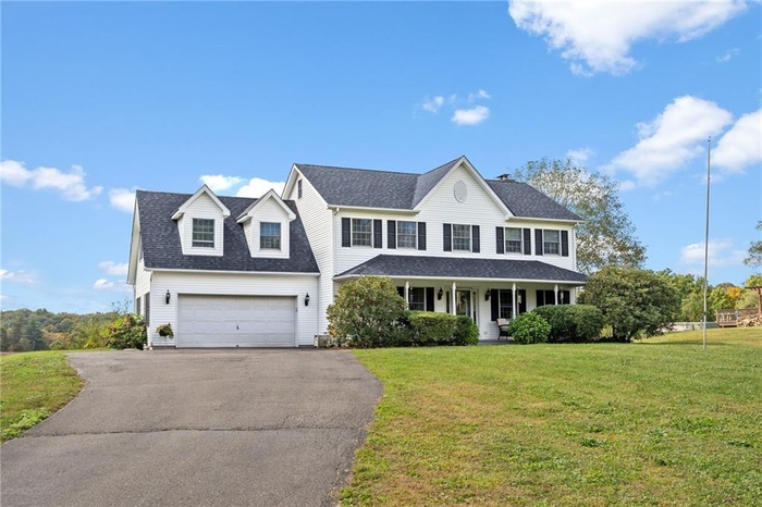 Colonial inspired home featuring an attached garage, a front yard, roof with shingles, driveway, and covered porch