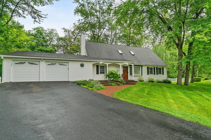 View of front facade with driveway, an attached garage, a chimney, a front yard, and a porch