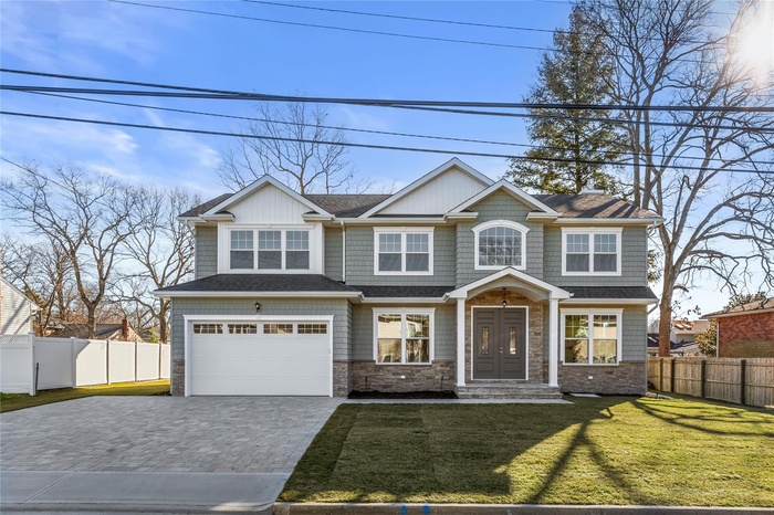 View of front facade featuring decorative driveway, an attached garage, stone siding, and a shingled roof