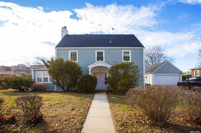 Colonial home featuring a chimney, a detached garage, an outdoor structure, and a front lawn