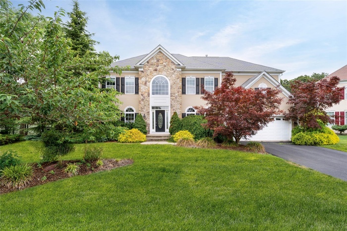Colonial inspired home with stone siding, driveway, a front lawn, and an attached garage