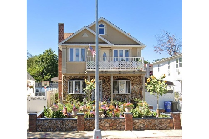 View of front facade with stone siding, a balcony, a chimney, and stucco siding