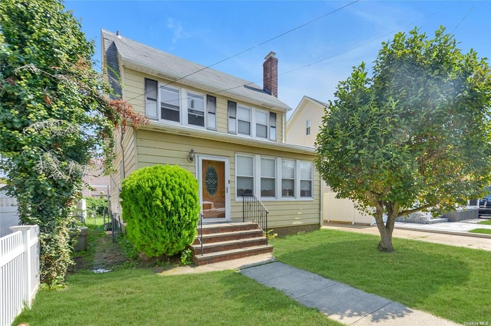 View of front of house with entry steps, fence, and a front lawn