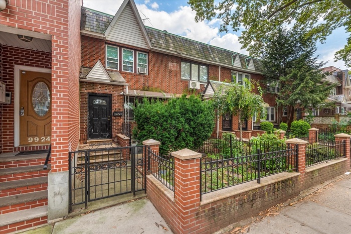 View of front of house with brick siding, a fenced front yard, mansard roof, and roof with shingles