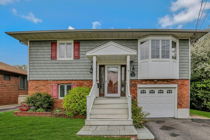 Raised ranch with brick siding, driveway, a front lawn, and a garage