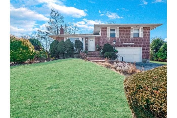 Tri-level home with a garage, driveway, a chimney, a front lawn, and brick siding