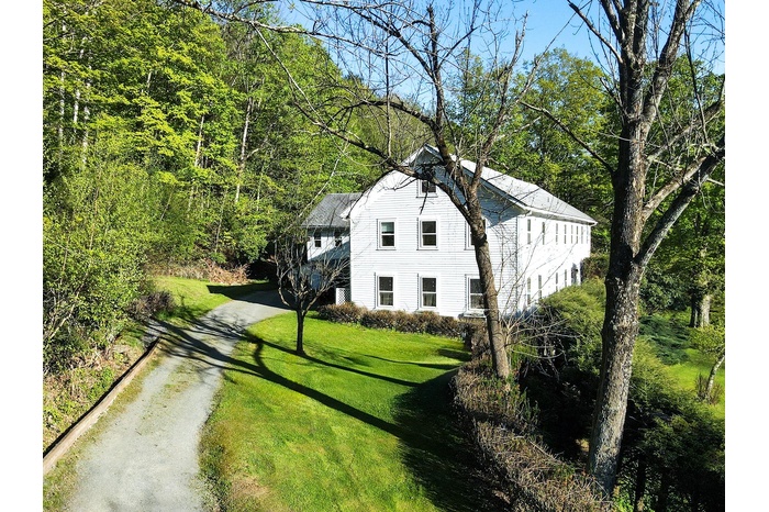 View of side of home with asphalt driveway, a lawn, and a wooded view