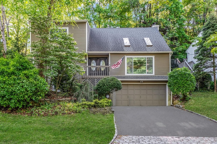 View of front facade featuring asphalt driveway, a shingled roof, a garage, and a front yard