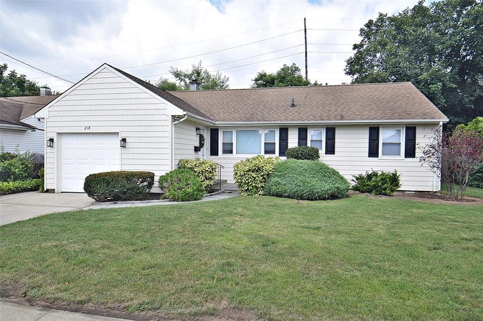 Ranch-style house with an attached garage, a front yard, roof with shingles, and driveway