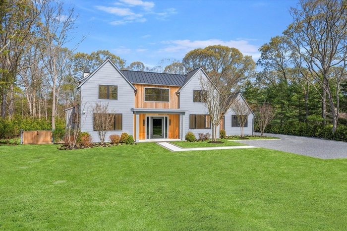 Modern farmhouse featuring a front lawn, a chimney, a standing seam roof, a metal roof, and driveway