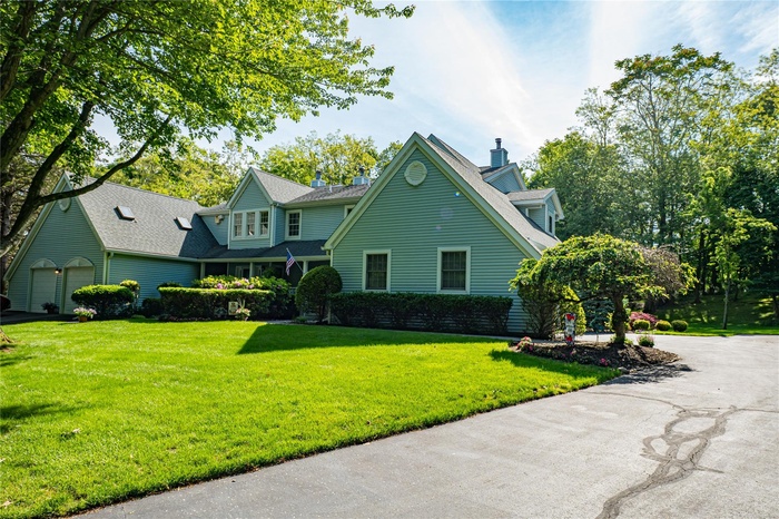 View of front of home with a chimney, driveway, a front lawn, and a shingled roof