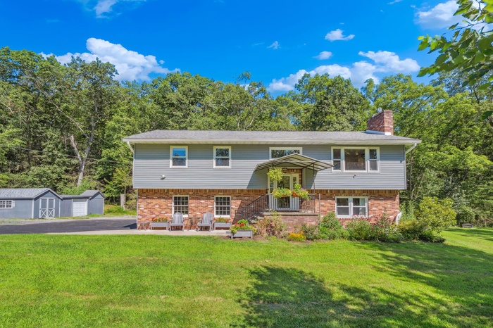 Split foyer home with brick siding, a storage unit, a front lawn, and a chimney