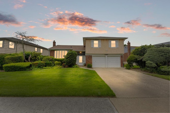 Split level home featuring brick siding, a garage, a chimney, concrete driveway, and a front yard