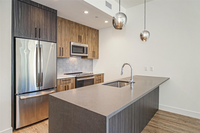Kitchen with appliances with stainless steel finishes, a peninsula, backsplash, light wood-style floors, and hanging light fixtures