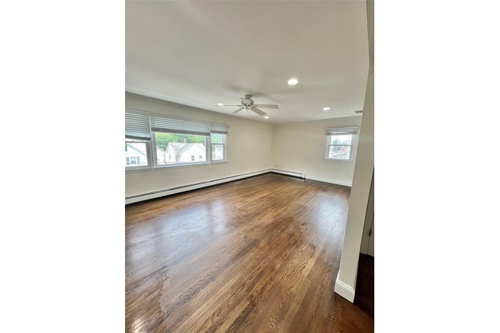 Living room with recessed lighting, dark wood-style floors, ceiling fan, and baseboard heating