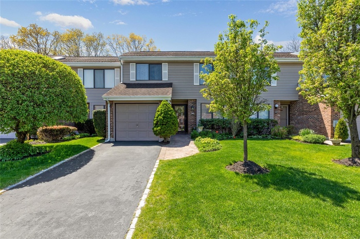 Multi unit property featuring an attached garage, aphalt driveway, a front lawn, and brick siding