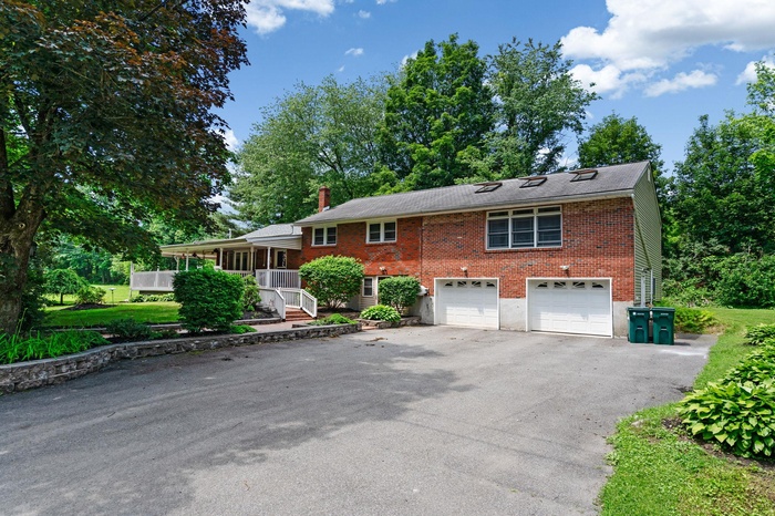 View of front of house with driveway, brick siding, an attached garage, and a chimney