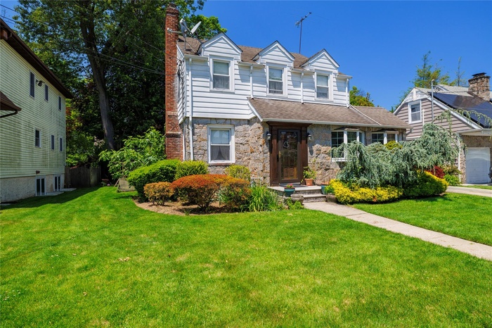 View of front facade featuring stone siding, a chimney, a front lawn, and a shingled roof