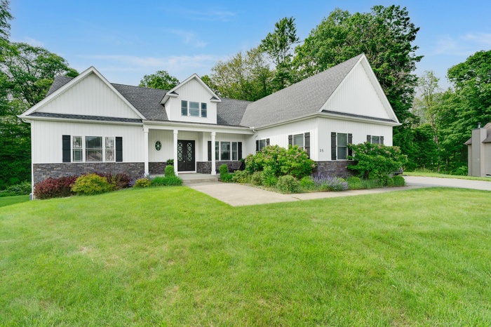 Modern farmhouse featuring stone siding, a front lawn, and roof with shingles