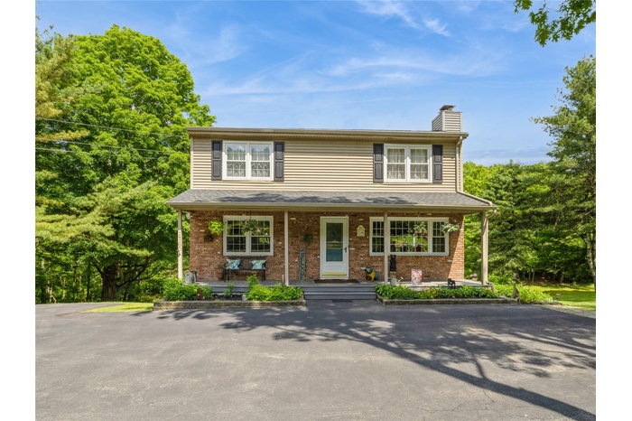 Traditional home with covered porch, a chimney, and brick siding