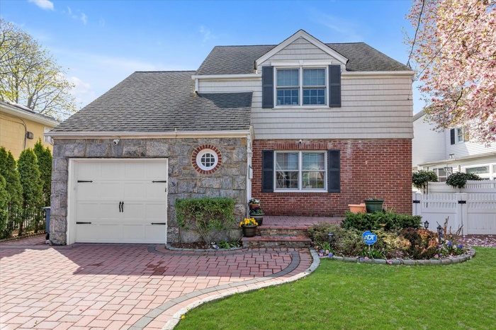 View of front of property featuring an attached garage, a front lawn, fence, and decorative driveway