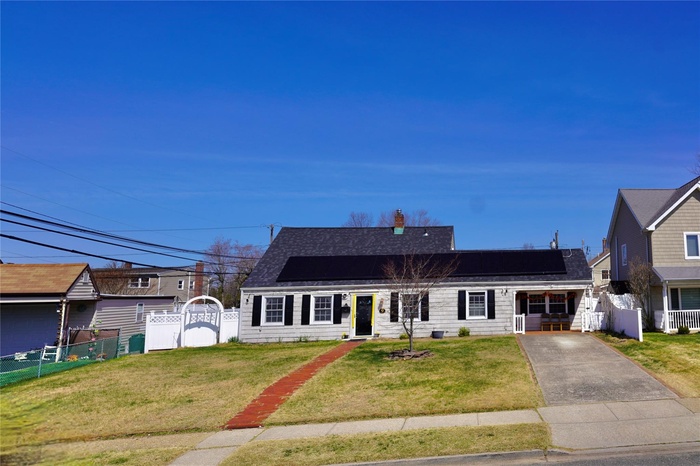 View of front facade with roof mounted solar panels, a gate, roof with shingles, and fence