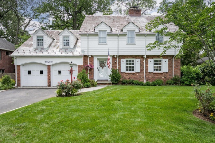 View of front of house with asphalt driveway, a chimney, a front lawn, and brick siding