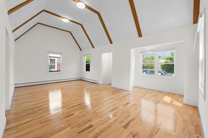 Unfurnished living room with baseboard heating, wood finished floors, a textured ceiling, and high vaulted ceiling