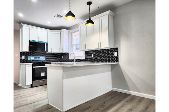 Kitchen with electric range, stainless steel microwave, wood finished floors, white cabinetry, and recessed lighting