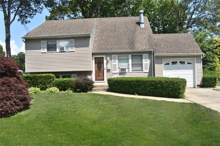 Tri-level home with a garage, concrete driveway, a front yard, and roof with shingles