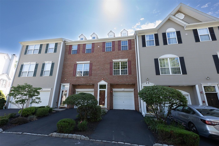 Townhouse style condo with attached garage, driveway, and brick siding