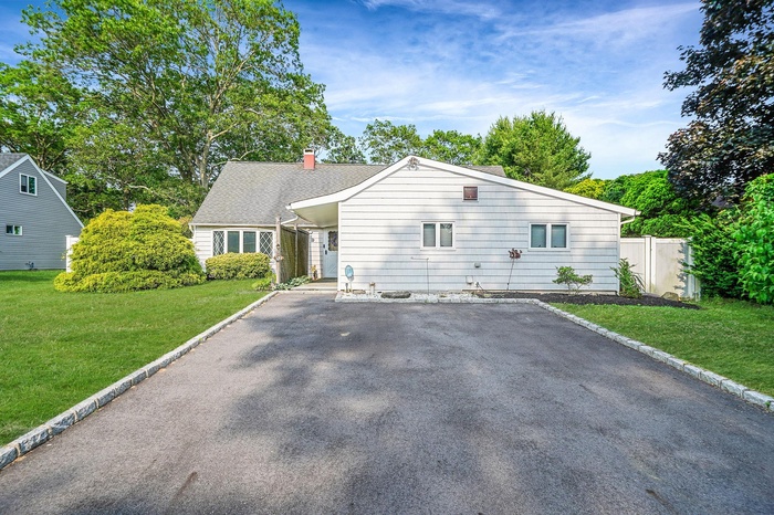 View of front of house with a chimney, driveway, and roof with shingles