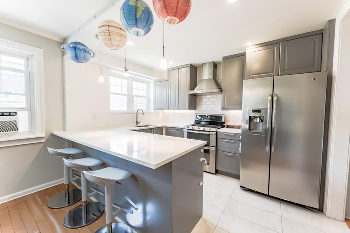 Kitchen with stainless steel appliances, gray cabinets, a peninsula, wall chimney range hood, and ornamental molding