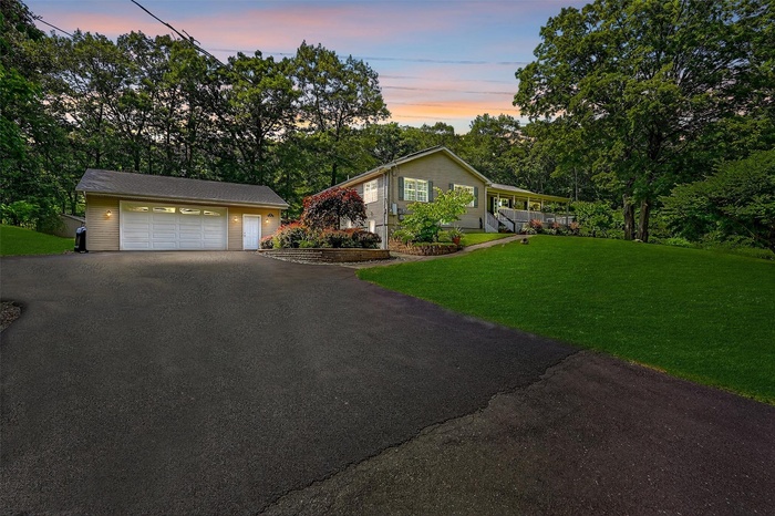 Single story home featuring a two car garage, view of wooded area, a front yard, and driveway