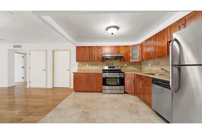 Kitchen featuring tasteful backsplash, light stone countertops, under cabinet range hood, stainless steel appliances, and a sink