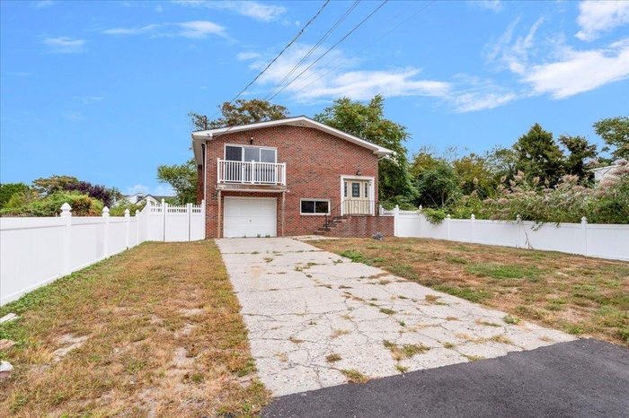 View of front of property featuring a garage, driveway, brick siding, and a balcony