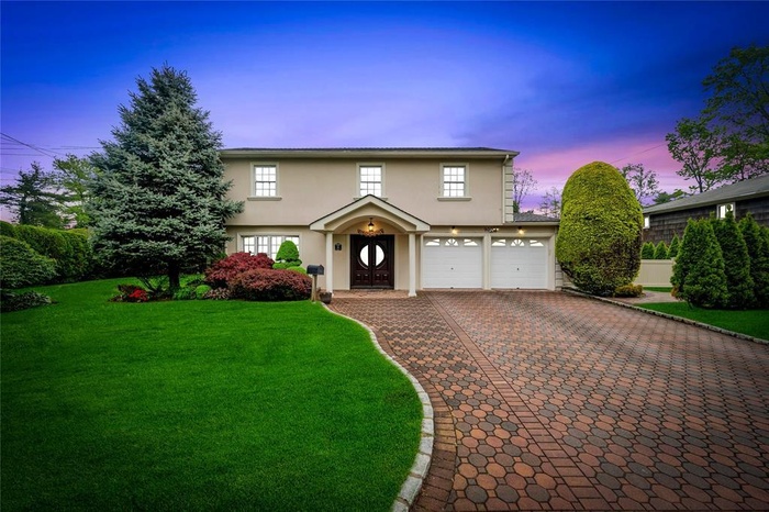 Traditional home featuring stucco siding, decorative driveway, an attached garage, and a yard
