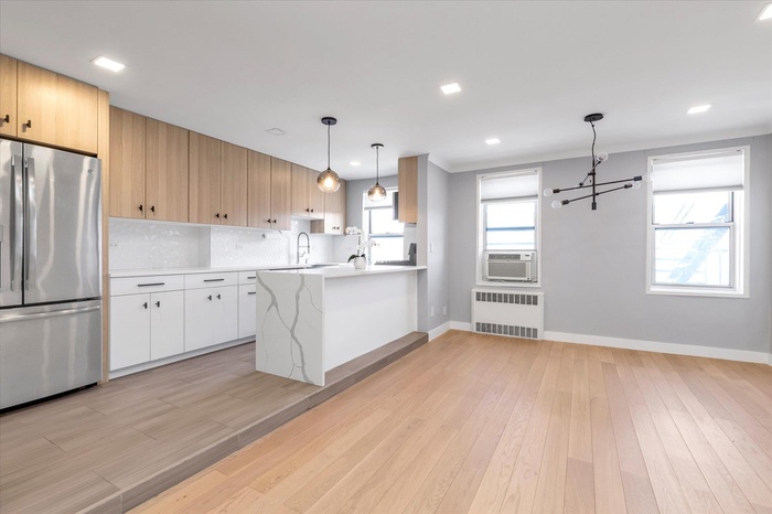 Kitchen featuring light wood-style flooring, a peninsula, light countertops, freestanding refrigerator, and radiator heating unit