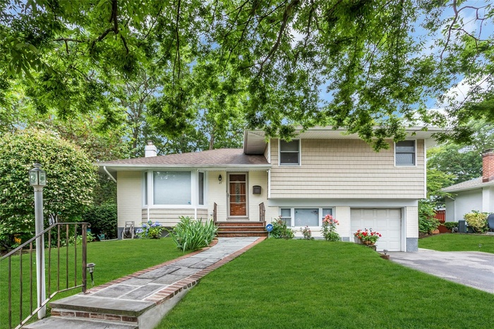 Tri-level home featuring a garage, driveway, a front lawn, and a chimney