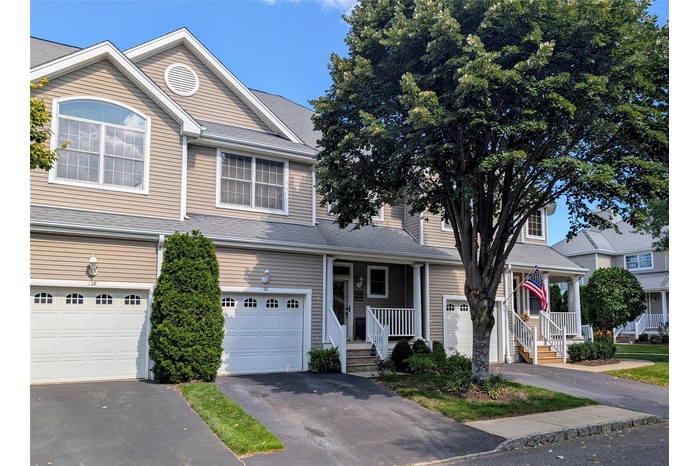 Traditional home featuring covered porch, driveway, a garage, and a shingled roof