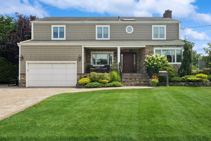 View of front of property featuring stone siding, a front yard, driveway, an attached garage, and a chimney