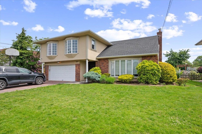 View of front of home with a chimney, driveway, brick siding, a garage, and stucco siding